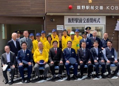 市長、スーツを着た男性、黄色いジャンパーを着た参加者の方々が集まって飯野駅前交番前で撮影した集合写真