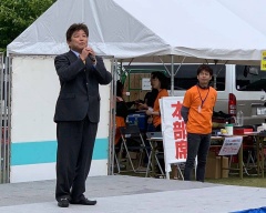 テント横に設置されたステージ上でマイクを持って話をしている市長の写真