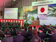 日本国旗の飾られたステージの講演台に立ってスピーチをしている市長とパイプ椅子に座っている大勢の自衛官、会場右側のパイプ椅子に座っている参加者の方々の写真
