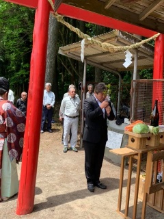 お供え物がされてある赤い鳥居の前で手を合わせているスーツ姿の市長と、装束を着た神主、関係者の方々が写っている馬頭観音祭での神事の様子の写真