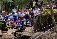 大きな岩を乗り越えようとするバイクに乗ったライダーと、観戦している大勢の観客の写真