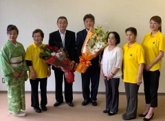 花束を持っている市長とスーツの男性、黄色のシャツを着ている3名の女性、着物を着ている女性、白いブラウスの女性の記念写真