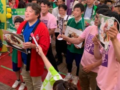 料理の写真パネルを持った赤い半被をきた男性を先頭に緑やピンクのシャツをきて料理の写真パネルをもって立っている大勢の参加者の写真