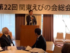関東えびの会総会と書かれた横断幕前に設置されたステージでマイクを持ち話をしている市長と着席して話を聞いている2名の男性の写真