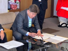 ガラスのテーブルにおかれた協定書にサインをしている市長の写真