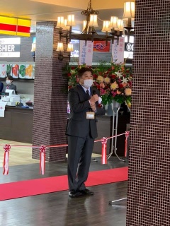 床に敷かれた赤いカーペット、お祝いの花、シャンデリア風の電灯の下でマイクをもって立っている市長の写真