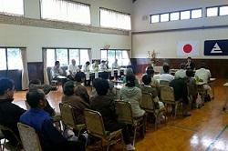 壁に日本国旗、えびの市旗が掲げられている会場で市長が座っている参加者達に話をしている写真