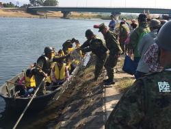 川にボートを浮かべ、黄色のライフジャケットを着用し乗っている参加者と陸上から指示している自衛官の写真
