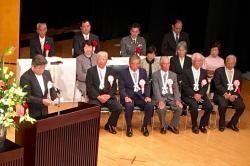 左側の演台に立って話をするえびの市長、右側に表彰された人たちが座っている写真