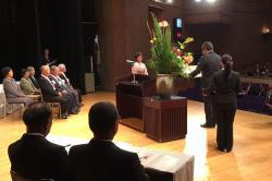 大きな花瓶に入った花が飾られている舞台中央にえびの市長が立っている表彰式の写真