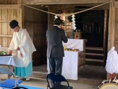 しめ縄の下の神棚の前で手を合わせている市長と、玉串が置かれたテーブルの前に立っている神主の写真