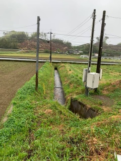 田畑の間を流れる用水路と電柱に設置された装置の写真