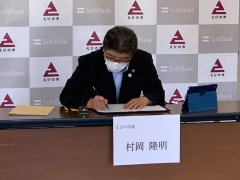 長机に置かれた資料にサインをしている眼鏡をかけた市長の写真
