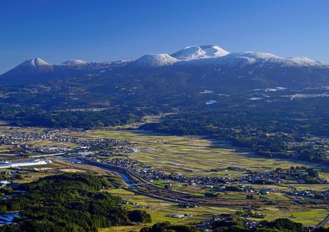 雪化粧をした山脈と田畑や川、民家が写っている風景を上空から写した写真
