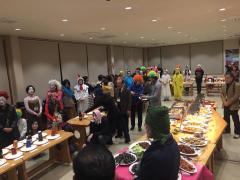 料理が置いてあるテーブルの周りを囲んでいる仮装をしている多くの参加者の写真
