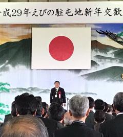 会場前方の日本国旗の下に立ち、話をしている市長と、市長の方を向いている大勢の参加者を後方から写した写真