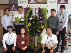 菊のアレンジメントの周りに集まる市長や、男女の記念写真