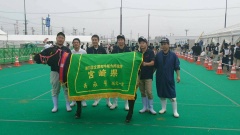 宮崎県と書かれた緑の幕を付けた牛と、その後ろに並ぶ6名の男性の記念写真