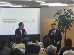スクリーンの前で市長と村岡さんがそれぞれマイクを持ってお客さんの前で話をしている写真