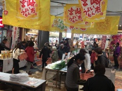 物産フェアで野菜や特産物が並び訪れた人々が買い物かごを持って歩いている写真