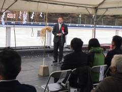 胸章リボンをつけた市長がアイススケート場で挨拶をしている写真