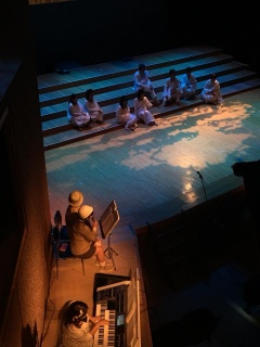 舞台の上が階段の様になっていて白い衣装を着た役者たちが座っている写真