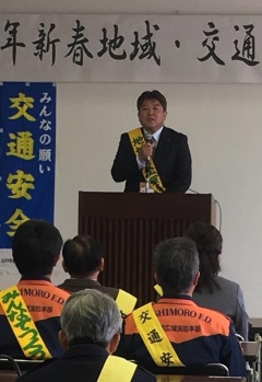 後ろの壁に交通安全と幕がかけられていて、黄色いタスキをかけた市長が参加者たちに向かって話をしている写真