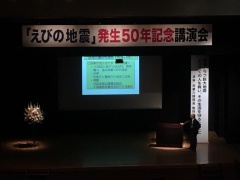 上にえびの地震発生50年記念講演会と幕があり、下には大きなスクリーンが置かれている講演会の写真