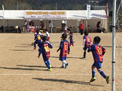 青に赤の縦じまの線が入ったユニフォーム姿の子供たちがサッカーをしている写真