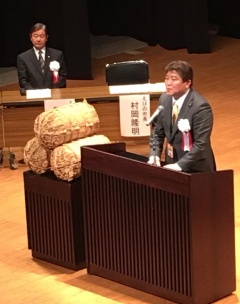 横に米俵が置かれている講演台でえびの市長が話をしている写真