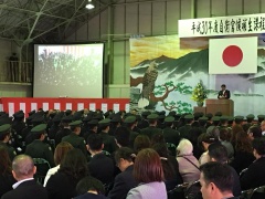 奥には舞台、手前には軍服を着た隊員たちや関係者たちが座っている入隊式の様子を写した写真