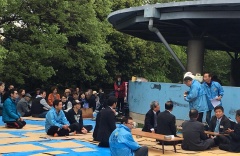 えびの市長、青い上着を着た男性達、スーツ姿の男性達がブルーシートの上に座っている写真