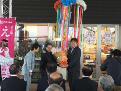 くす玉の下で、市長が男性に花束を渡している写真