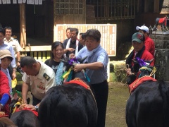 牛の綱を握っている市長と周りに立っている赤い法被を着ている男性や見ている大勢の観客の写真