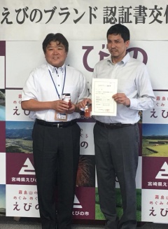 ピペラードの入った瓶を持つ市長と、ブランド認証書を持つ岡田さんが並んでいる写真
