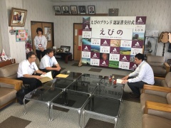 中央にあるテーブル上にピペラードの瓶、資料が置かれ、市長と関係者、岡田さんが向かい合って座っている写真