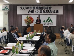 日本国旗とJAえびの市の旗が掲げられた舞台上で市長が参加者にむけて話をしている写真