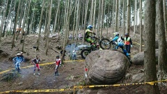 林の中にある大きな岩の上をヘルメットを被った選手がマウンテンバイクで登っている大会の写真