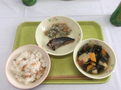 緑のお盆の上にご飯、魚のおかず、汁物が盛り付けられたお椀やお皿が置かれている写真