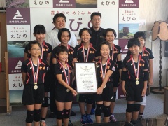 首にメダルをかけユニフォーム姿の加久藤少女バレー部の選手たちと市長、関係者が並んでいる写真
