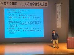 舞台の右側に黒田代表、中央には文字が映っている大きなスクリーンが置かれている講演会の写真