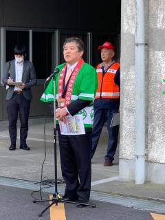 緑の法被を着た市長が、マイクの前に立って挨拶をしている写真