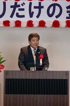 胸に赤い花をつけスーツを着た市長が話をしている写真