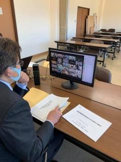 市長の座っている机にパソコンと資料が置かれていて、市長がリモート会議に出席している写真