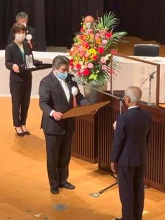 マスク姿の市長が向かい合っている表彰者の男性に賞状を渡そうとしている写真