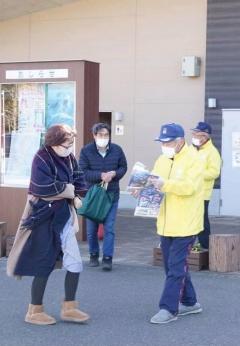 黄色い上着を着た男性が歩いている女性に交通安全のパンフレットを渡そうとしている写真