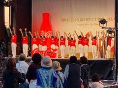 舞台上で、白いズボンに赤いシャツを着た女性達が、両手を上げて並んでいる写真