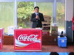コカコーラのロゴの机を前にマイクをもって話をしている市長の写真