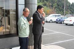 広い駐車場がある建物の前でソフトクリームを食べている市長と眼鏡をかけている男性の写真