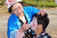 鉢巻を巻いた女性が、地元の方の化粧直しをしている写真